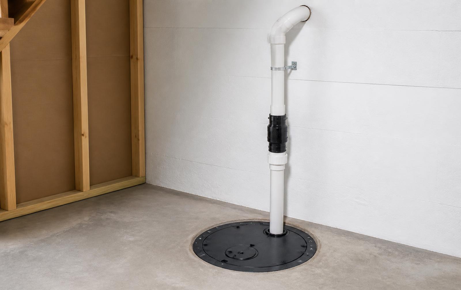 Sealed sump pit lid and white PVC discharge line in a clean, dry residential basement